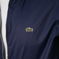 Détail d'une veste Lacoste élégante avec logo emblématique sur fond bleu.